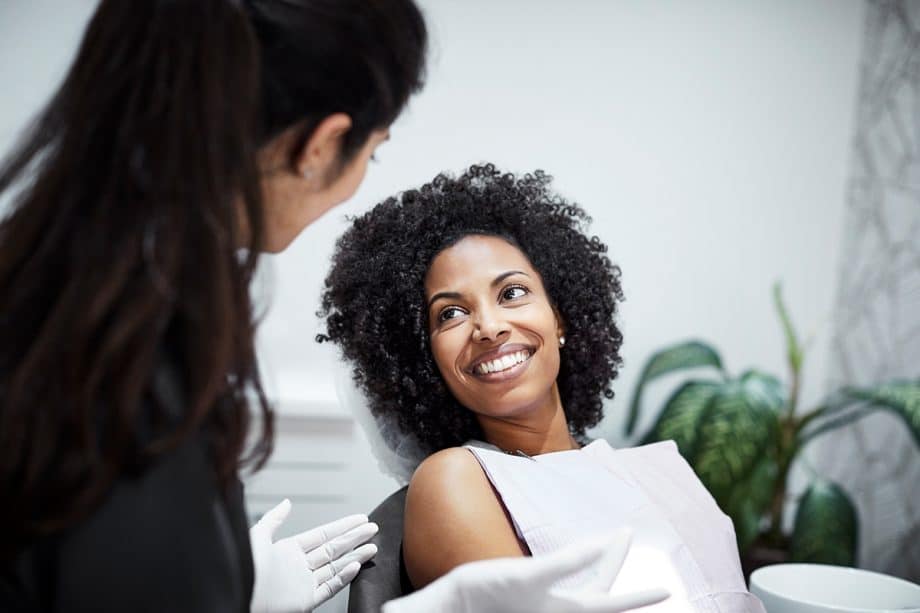 woman in dental chair smiles and shows her dental veneers