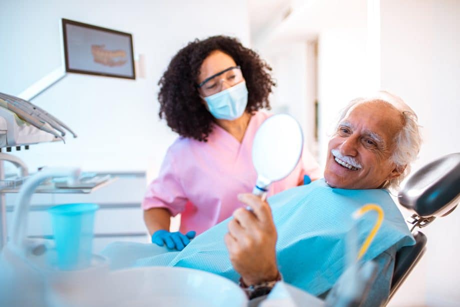 smiling man in dental chair examines dental veneers in a hand mirror